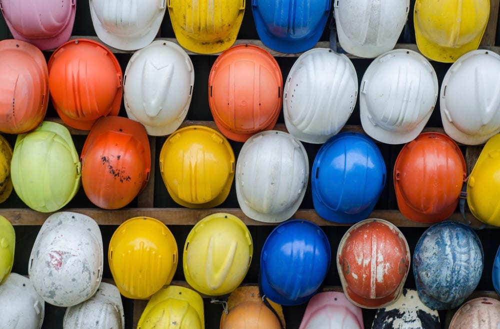 Rows of well-used hard hats on racks, in yellow, white, orange and blue.